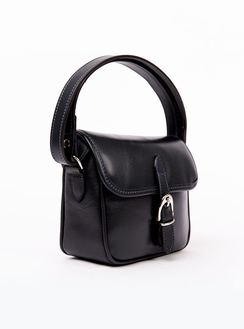 Flat lay of a small premium bridle butt navy leather crossbody Faith hand bag that has been hand stitched in England with 1 front facing buckle strap and the back embossed with Newmarket 875 horse logo.