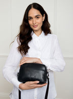 Woman wearing a large premium bridle butt navy leather Bridget crossbody camera hand bag that has been hand stitched in England with red threading and embossed with the Newmarket 875 brand horse logo.
