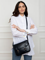 Woman wearing a large premium bridle butt navy leather crossbody Ceres hand bag that has been hand stitched in England with 2 front facing buckle straps and embossed with the Newmarket 875 horse logo on the back.