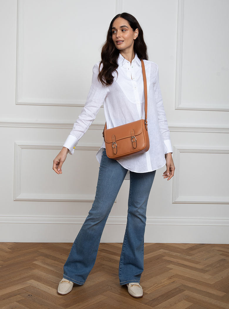 Woman wearing a large premium bridle butt tan leather crossbody Ceres hand bag that has been hand stitched in England with 2 front facing buckle straps and embossed with the Newmarket 875 horse logo on the back.