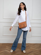 Woman wearing a large premium bridle butt tan leather crossbody Ceres hand bag that has been hand stitched in England with 2 front facing buckle straps and embossed with the Newmarket 875 horse logo on the back.