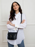 Woman wearing a small premium bridle butt navy leather crossbody Faith hand bag that has been hand stitched in England with 1 front facing buckle strap and the back embossed with Newmarket 875 horse logo.