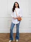 Woman wearing a small premium bridle butt tan leather crossbody Faith hand bag that has been hand stitched in England with 1 front facing buckle strap and the back embossed with Newmarket 875 horse logo.