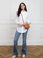 Woman wearing a small premium bridle butt tan leather crossbody Faith hand bag that has been hand stitched in England with 1 front facing buckle strap and the back embossed with Newmarket 875 horse logo.