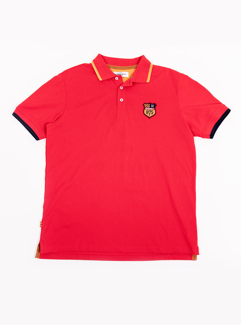 Flat lay of men's red polo shirt in 100% cotton with Newmarket 875 crest embroidered on the front with navy sleeve trimming and gold collar trimming.