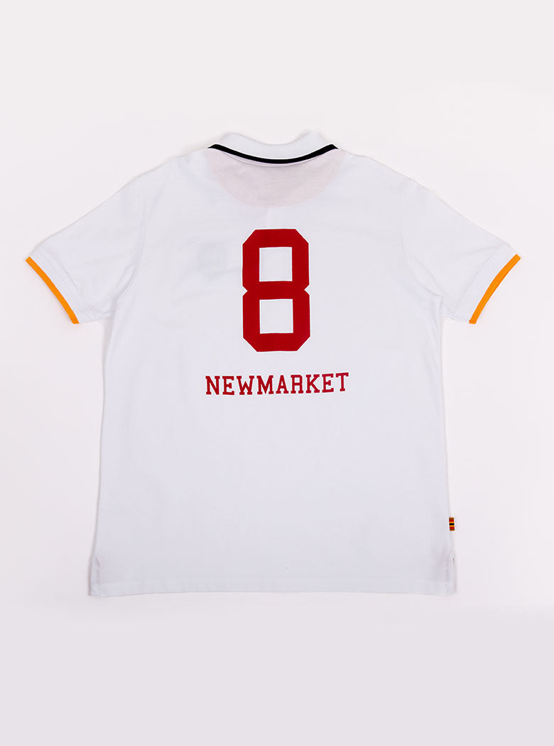 Flat lay of men's white polo shirt in 100% cotton with Newmarket 875 crest embroidered on the front and giant red 8 on the back with navy sleeve trimming and gold collar trimming.