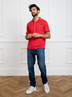 Man wearing red polo shirt in 100% cotton with Newmarket 875 crest embroidered on the front with navy sleeve trimming and gold collar trimming.