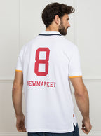Man wearing white polo shirt in 100% cotton with Newmarket 875 crest embroidered on the front with navy sleeve trimming and gold collar trimming.