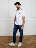 Man wearing white polo shirt in 100% cotton with Newmarket 875 crest embroidered on the front with navy sleeve trimming and gold collar trimming.