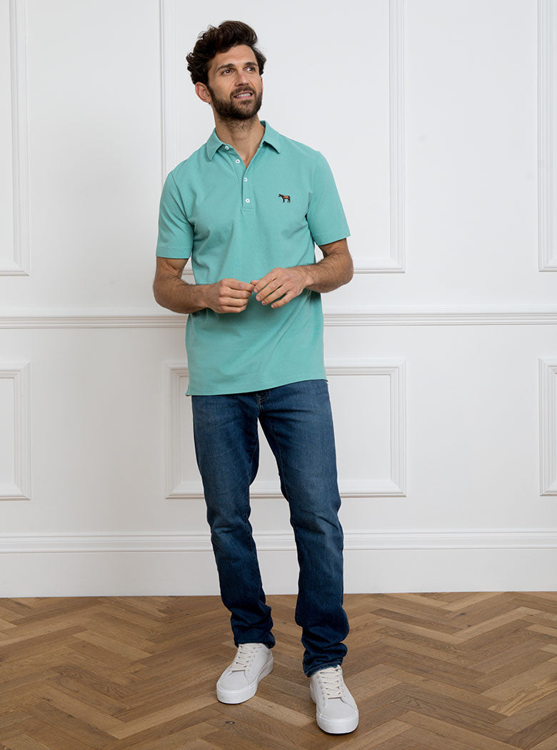 Man wearing avocado green polo shirt in 100% cotton with Newmarket 875 horse logo embroidered on the front.