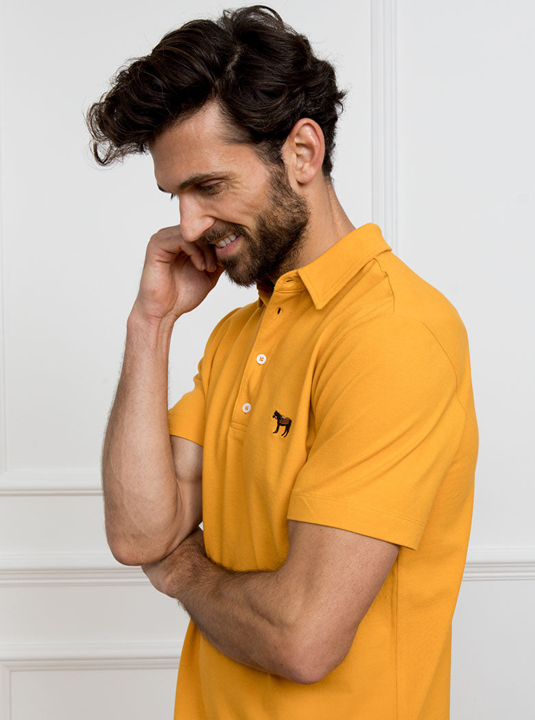 Man wearing gold yellow polo shirt in 100% cotton with Newmarket 875 horse logo embroidered on the front.