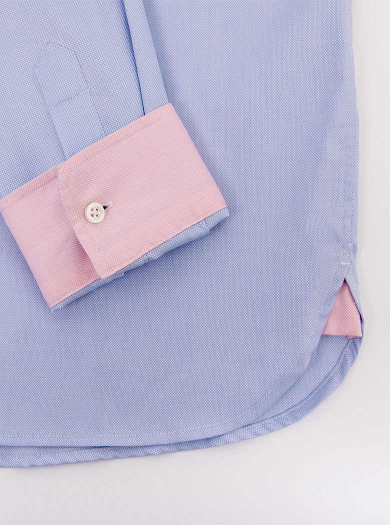 Flat lay of men's sky blue long sleeved shirt with a button down collar with inside of collar and cuff pale pink trimmings made with 100% cotton in a Thomas Mason fabric.