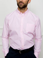 Man wearing a long sleeved shirt with a pale pink and white thin stripe pattern made with 100% Oxford in a Thomas Mason fabric.