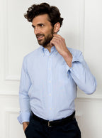 Man wearing long sleeved shirt with sky blue and white thin stripe and the inside collar and cuffs trimmed with gingham pattern. Made with 100% cotton in Thomas Mason fabric.