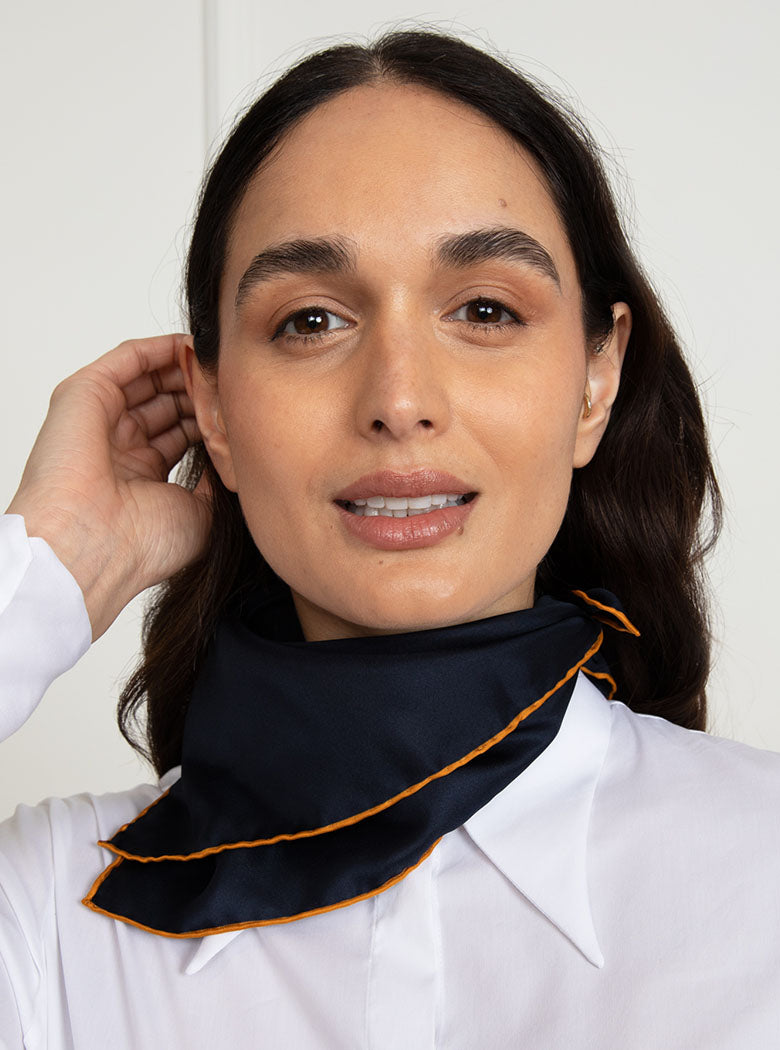 Woman wearing 100% silk 40x40 hank scarf in navy with gold yellow hand stitched border. 