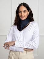 Woman wearing 100% silk 40x40 hank scarf in navy with gold yellow hand stitched border. 