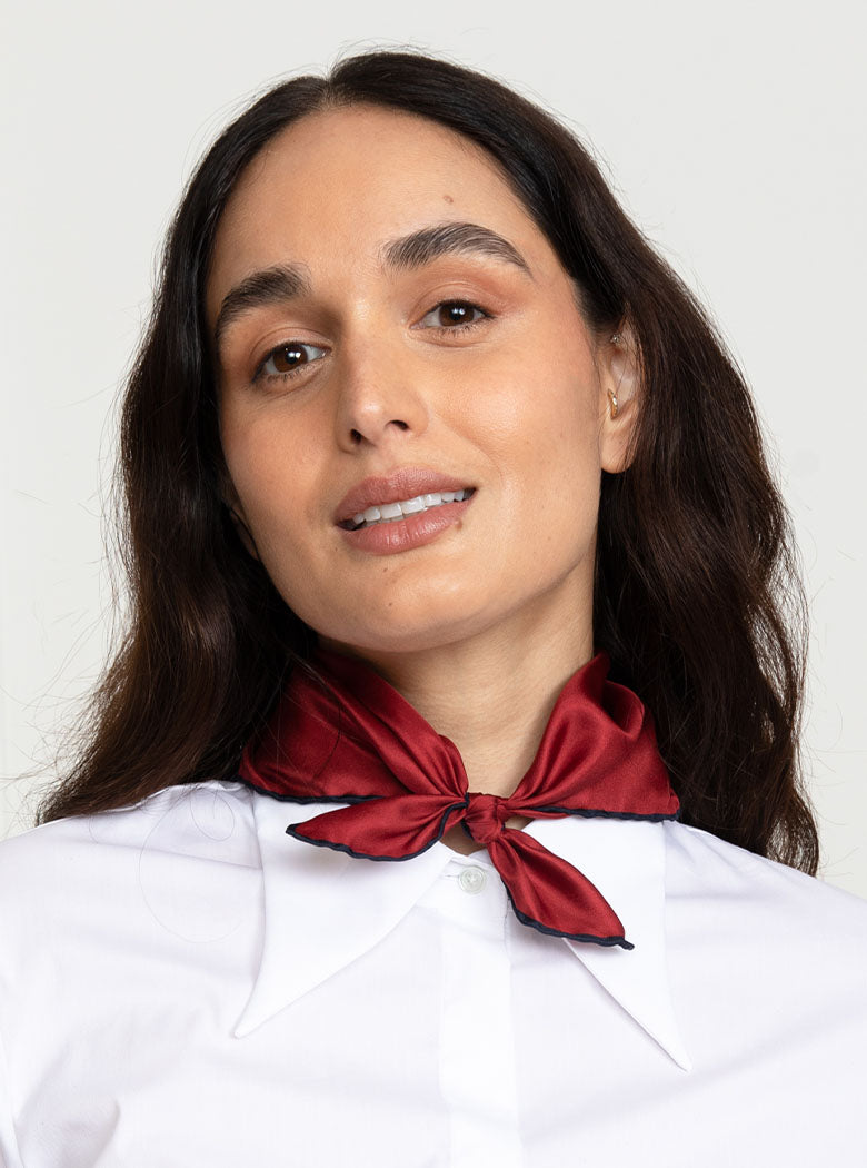 Woman wearing 100% silk 40x40 hank scarf in red with navy hand stitched border. 