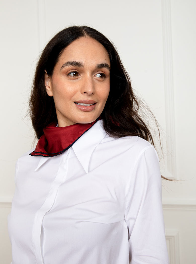 Woman wearing 100% silk 40x40 hank scarf in red with navy hand stitched border. 