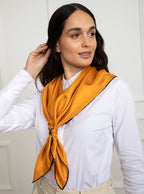 Woman wearing 100% silk 90x90 foulard scarf in gold yellow with navy hand stitched border. 