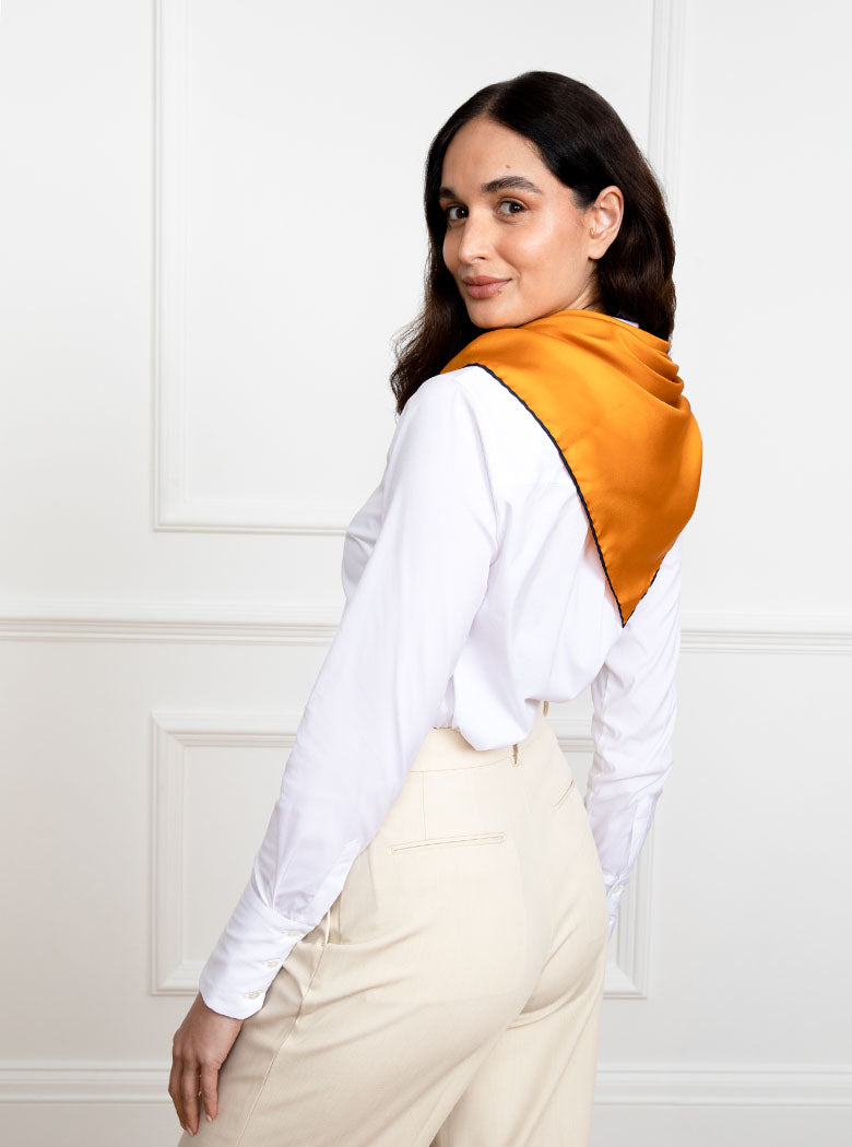 Woman wearing 100% silk 90x90 foulard scarf in gold yellow with navy hand stitched border. 