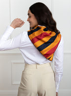 Woman wearing 100% silk 90x90 foulard scarf in traditional Newmarket red, navy, gold yellow stripe with navy hand stitched border. 